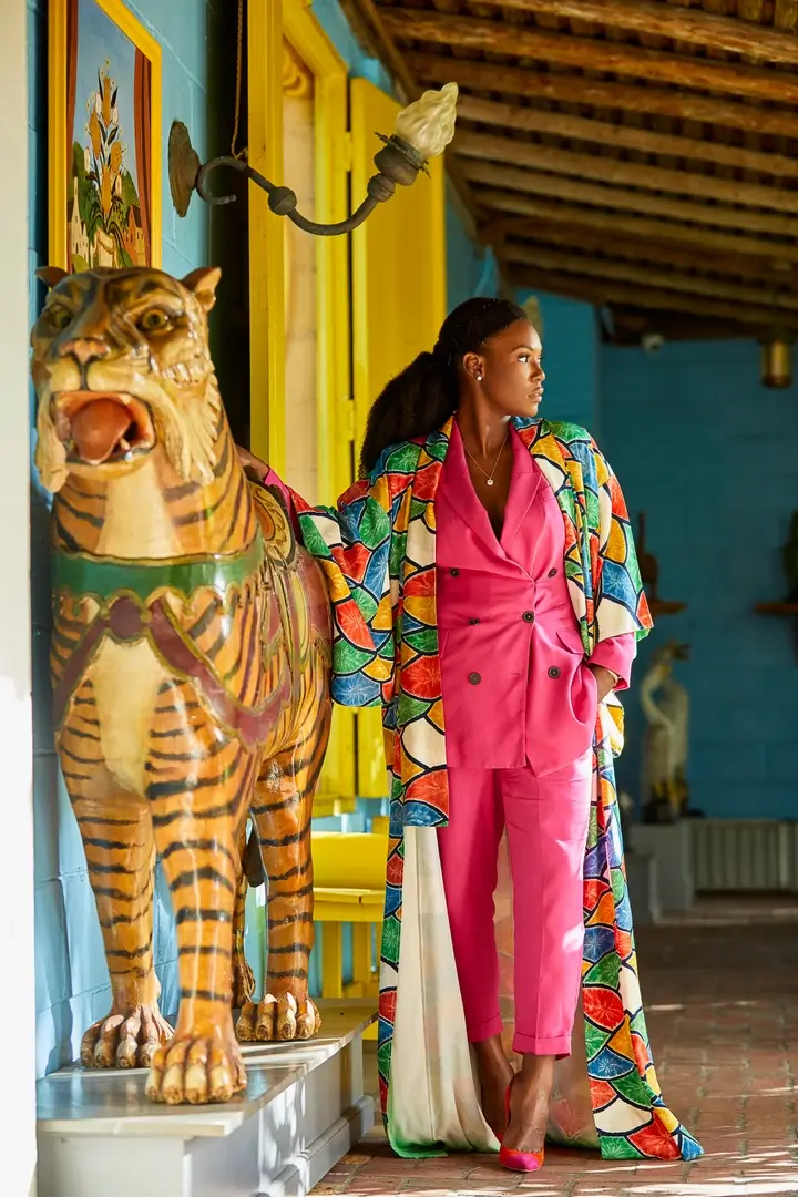 Toni Lowe in a pink suit and vivid patterned duster coat beside a painted tiger statue